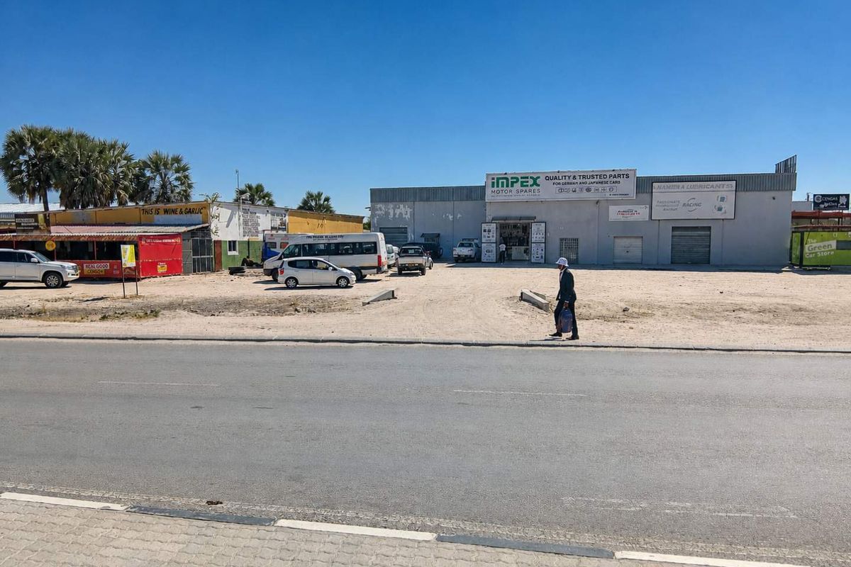 Street-level view of a commercial property featuring multiple business units, roller shutter doors, and an unpaved parking area.