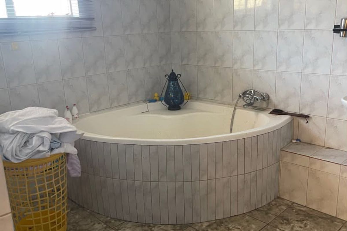 A bathroom featuring a corner bathtub with tiled surround and flooring, offering a functional layout with natural light from the window.