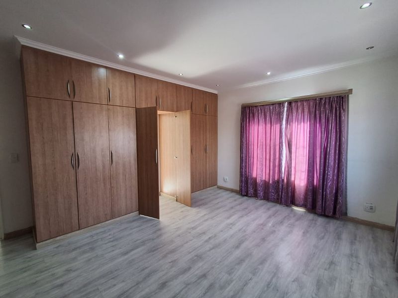 Spacious bedroom featuring extensive built-in wooden cupboards, modern laminate flooring, and recessed ceiling lighting.