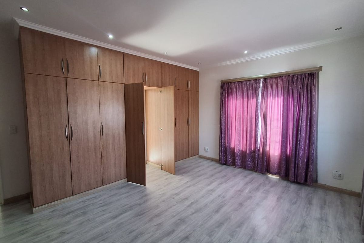 Spacious bedroom featuring extensive built-in wooden cupboards, modern laminate flooring, and recessed ceiling lighting.