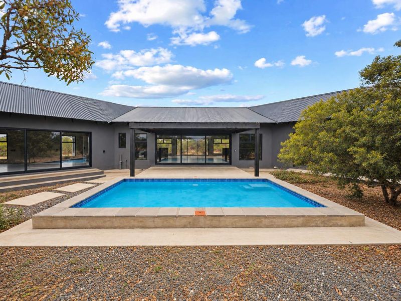 A modern outdoor pool area featuring a rectangular swimming pool, a covered patio space, and large sliding glass doors leading into the home.
