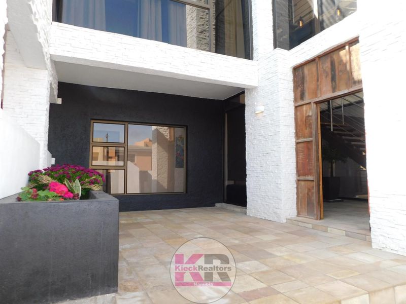 Modern covered patio area featuring stone-clad walls, tiled flooring, and a large timber-framed entrance leading into the home.