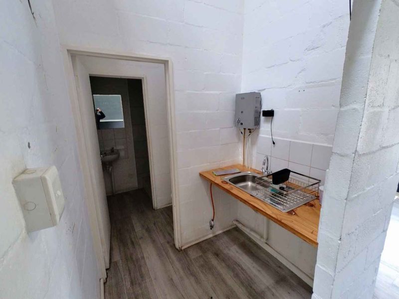 A functional scullery or utility area featuring a stainless steel sink, wooden countertop, and exposed blockwork walls, providing basic prep and wash-up facilities.