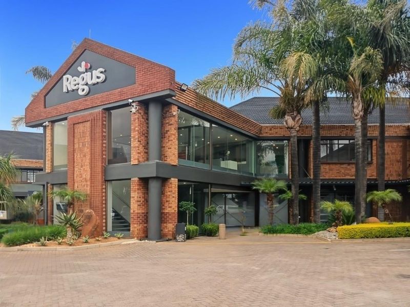 A professional front exterior view of a modern brick office building featuring large glass windows, a paved driveway, and well-maintained landscaping.