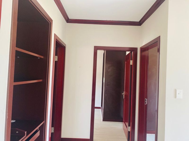 A bright hallway featuring dark wood door frames, matching crown molding, and built-in shelving units, providing access to adjacent rooms.