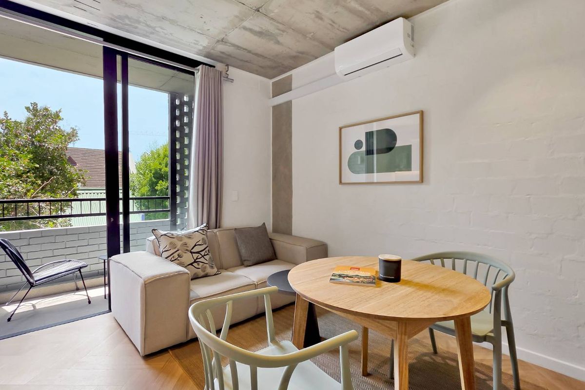 Modern living area featuring an exposed concrete ceiling, herringbone timber flooring, and direct access to a private balcony through sliding glass doors.