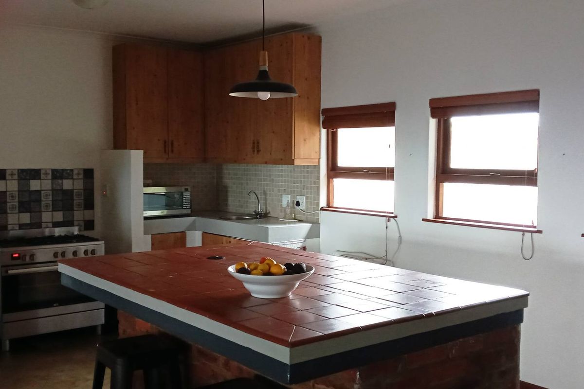 A functional kitchen featuring wooden cabinetry, a tiled island countertop, built-in stove, and tiled backsplash, offering a practical layout with natural light.