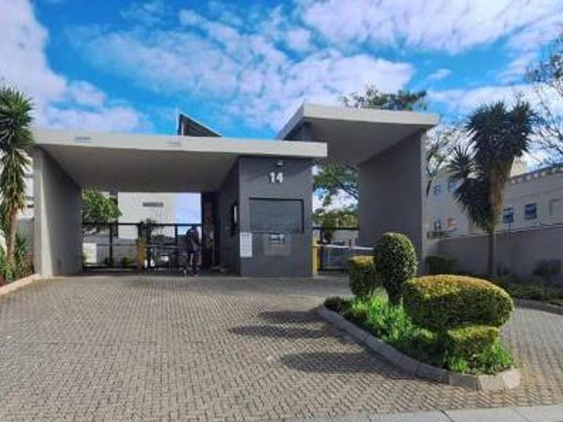The main entrance and security gatehouse of the apartment complex, featuring a paved driveway and well-maintained landscaping.