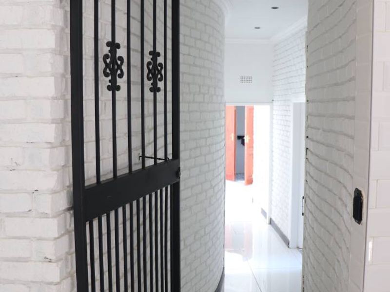 A bright, modern hallway featuring white painted brick walls, a curved architectural design, polished tiled flooring, and a black metal security gate.