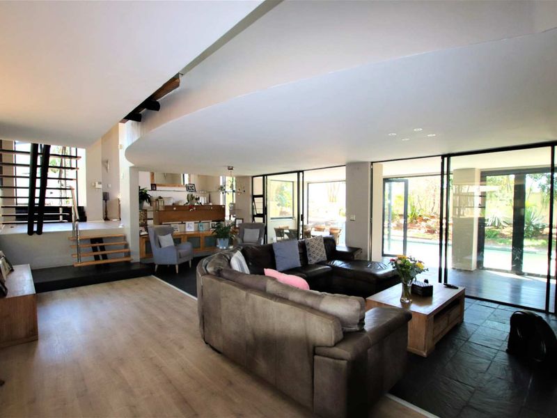 Spacious open-plan living area featuring a modern floating staircase, slate and laminate flooring, and large sliding glass doors opening to the outdoor pool area.