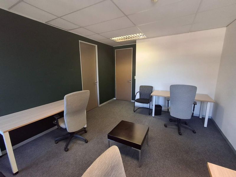 A functional office space featuring carpeted flooring, a suspended ceiling with recessed lighting, and two internal doors.