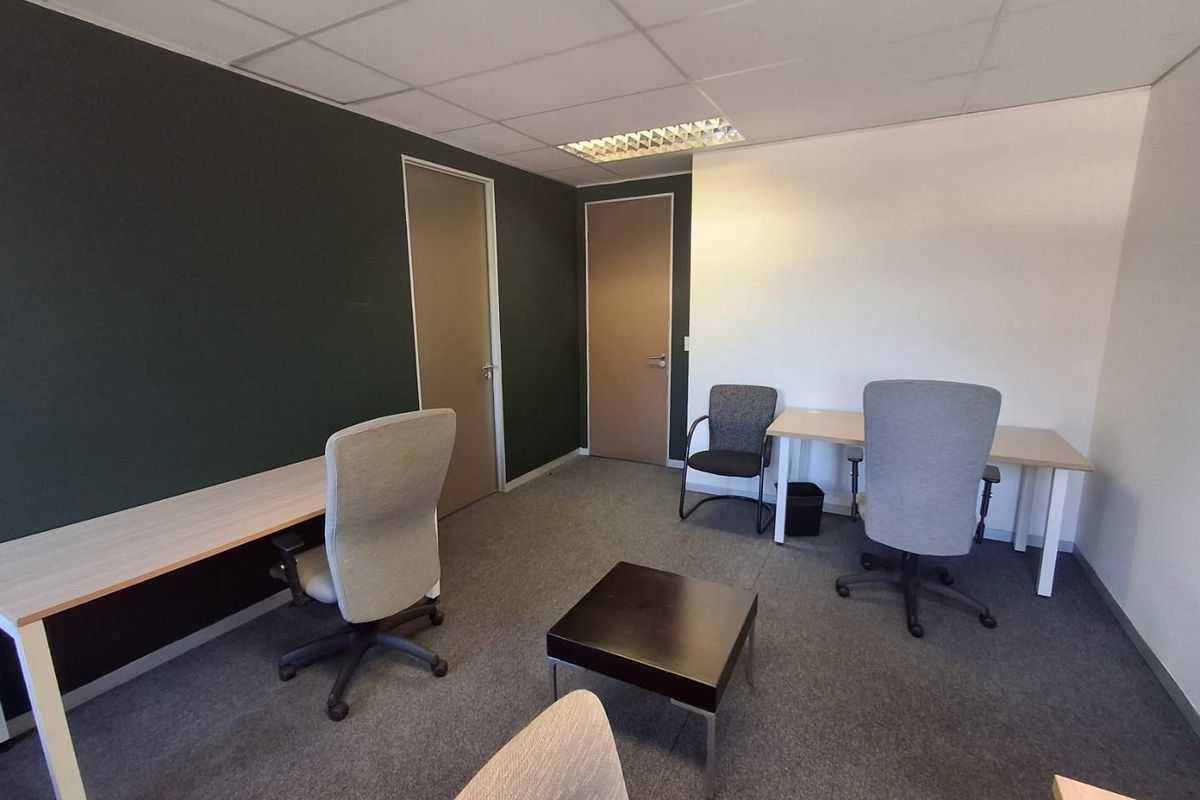 A functional office space featuring carpeted flooring, a suspended ceiling with recessed lighting, and two internal doors.