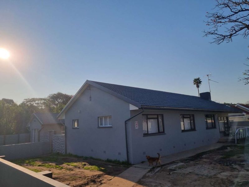 Rear view of a single-story house featuring a tiled roof, grey exterior walls, and aluminium window frames with an adjacent concrete pathway.