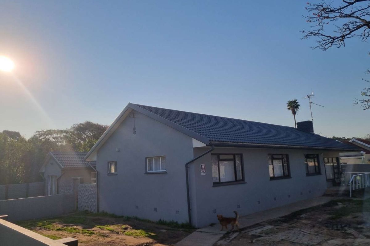 Rear view of a single-story house featuring a tiled roof, grey exterior walls, and aluminium window frames with an adjacent concrete pathway.