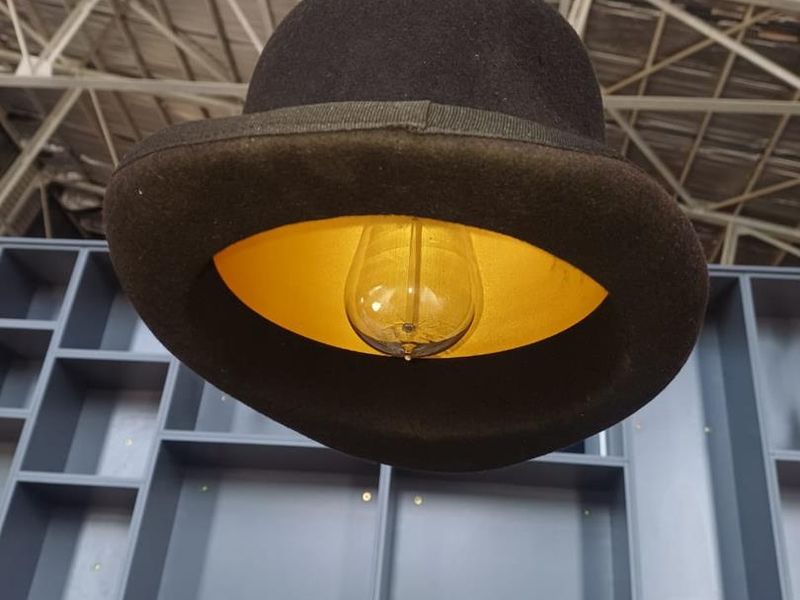 Close-up of a decorative hat-style pendant light fixture suspended in front of a grey built-in shelving unit with an exposed industrial ceiling.