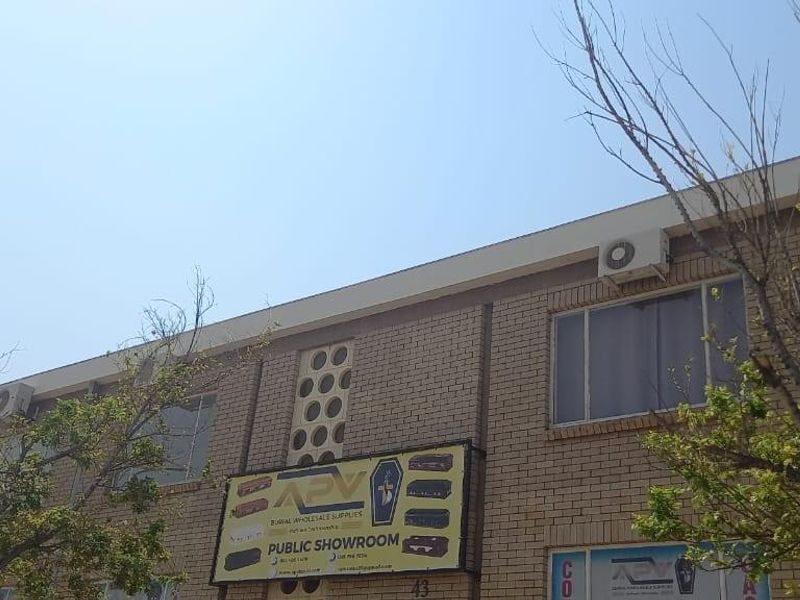 Exterior view of a two-story brick office building featuring large windows, mounted air conditioning units, and prominent commercial signage.