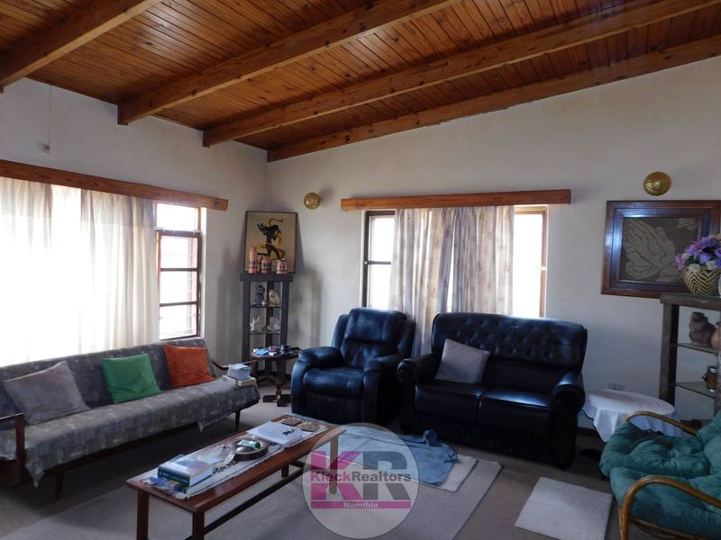 A living room featuring a high exposed timber beam ceiling and large windows, offering a rustic aesthetic with potential for modern updates.