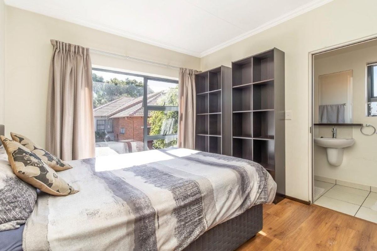 A bedroom featuring laminate flooring, aluminium window frames, and an attached en-suite bathroom with neutral wall finishes.