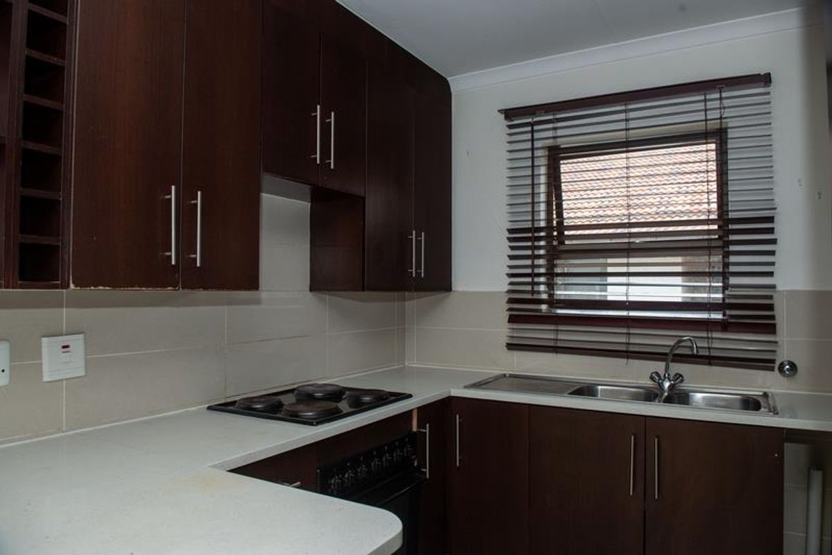 A functional kitchen featuring dark wood cabinetry, a built-in electric hob and oven, a double stainless steel sink, and a window with fitted blinds.