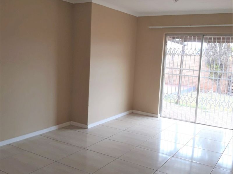 An empty, tiled living room featuring a sliding glass door with a security gate, providing access to the outdoor area.