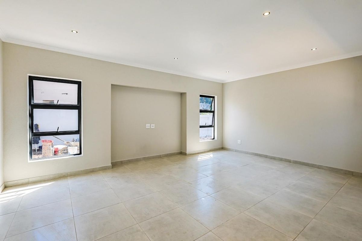 A bright, spacious, and empty living area featuring neutral tiled flooring, recessed ceiling lighting, and modern black-framed windows.