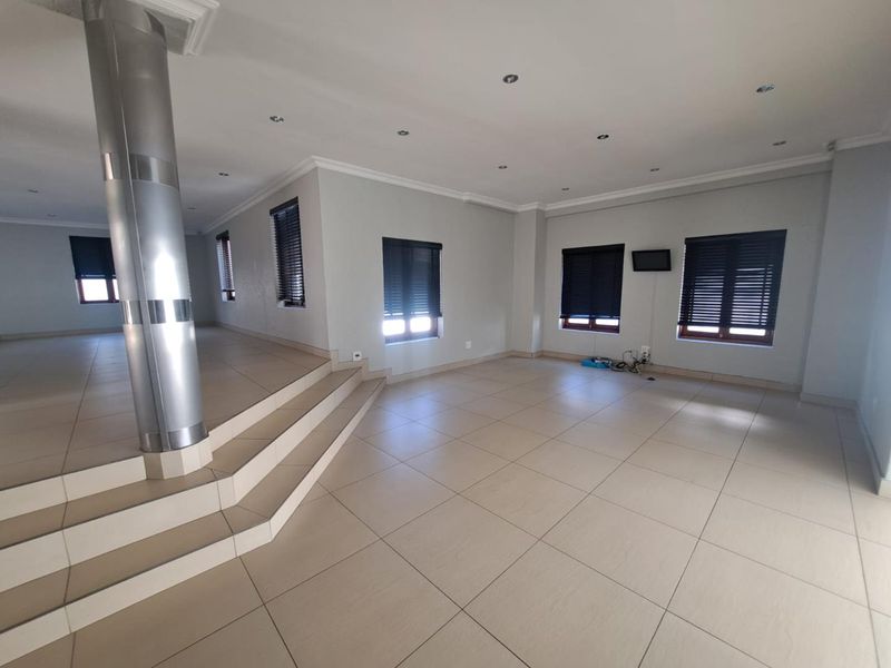 Spacious, open-plan living area featuring large format floor tiles, a raised platform with a central support column, and modern recessed lighting.