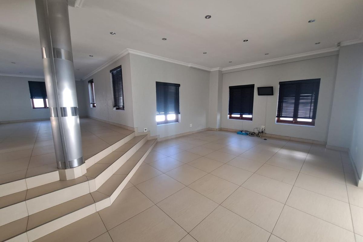 Spacious, open-plan living area featuring large format floor tiles, a raised platform with a central support column, and modern recessed lighting.