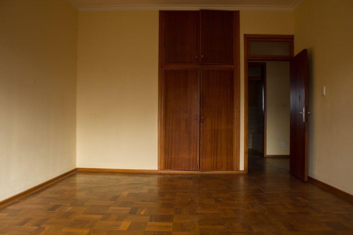 An empty bedroom featuring classic parquet flooring and built-in wooden cupboards, offering a blank canvas for renovation or interior design updates.