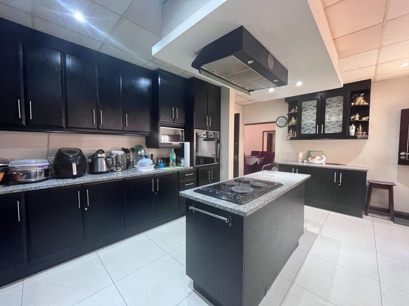 Modern kitchen featuring dark cabinetry, granite countertops, a central island with a built-in cooktop, and a stainless steel extractor fan.