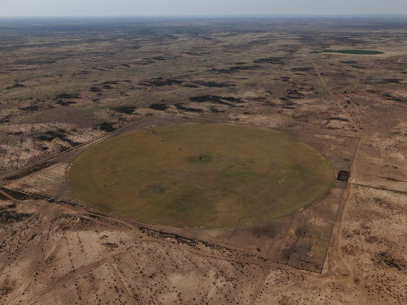 Aerial view of a large circular irrigated crop field situated within a vast arid farm landscape.