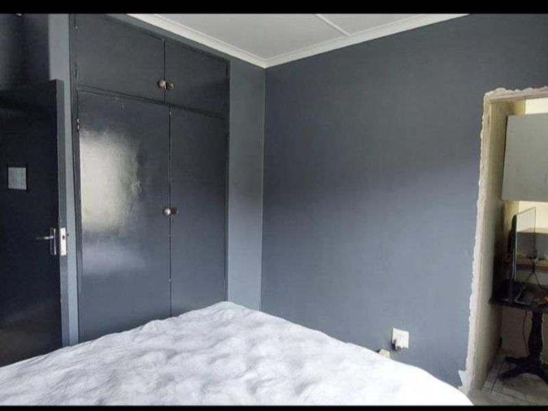 A bedroom featuring dark grey walls and built-in cupboards, with an unfinished doorway leading to an adjacent room.