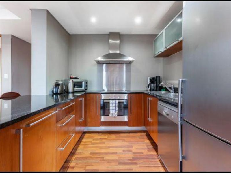 A well-maintained kitchen featuring wooden cabinetry, granite countertops, a built-in oven with extractor fan, and integrated stainless steel appliances.