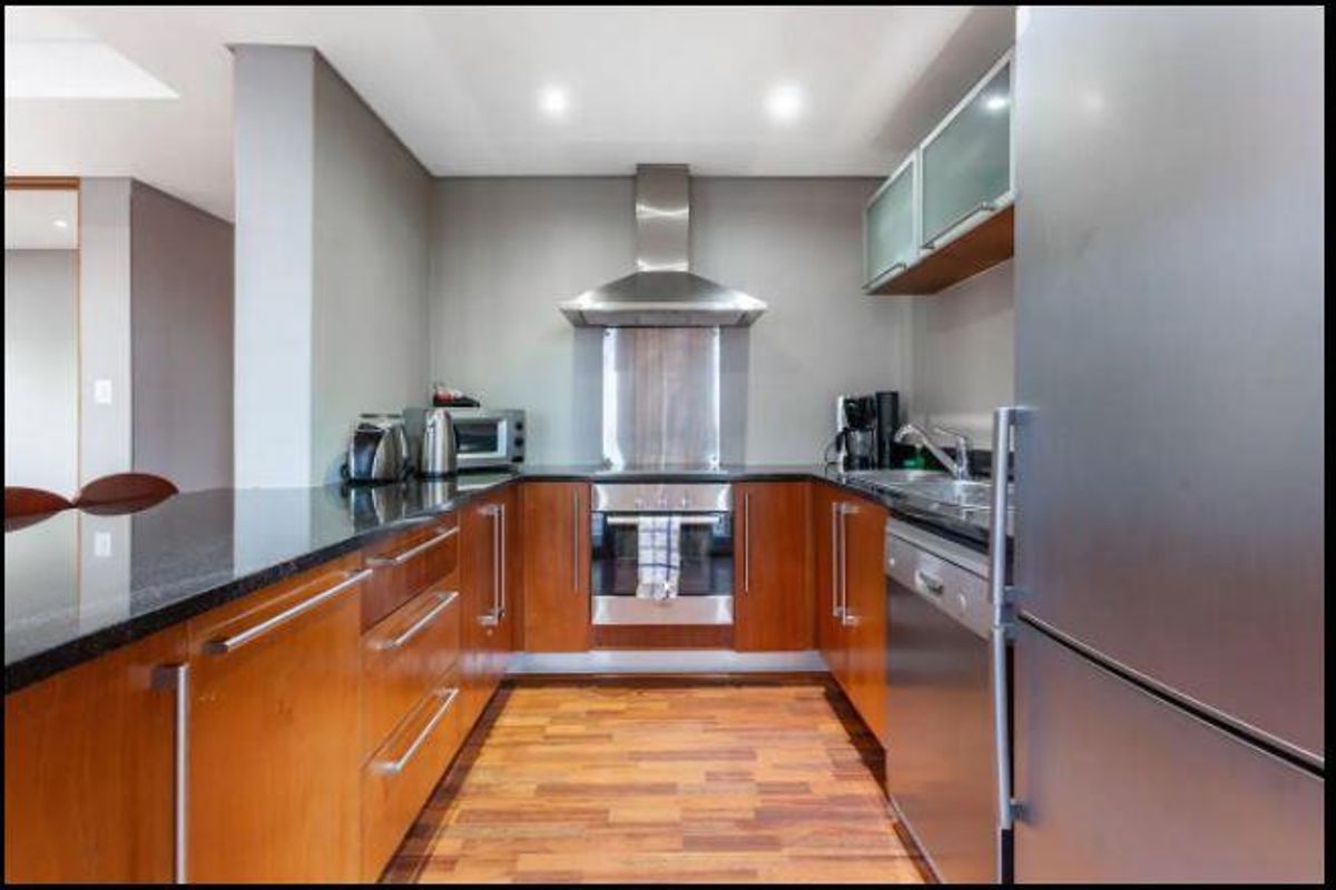 A well-maintained kitchen featuring wooden cabinetry, granite countertops, a built-in oven with extractor fan, and integrated stainless steel appliances.
