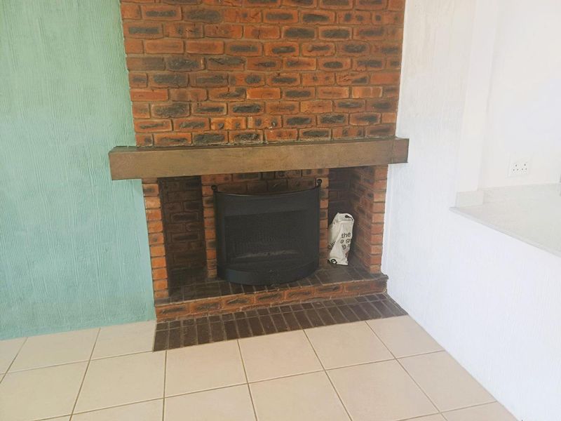 A living room area featuring a traditional brick fireplace with a mantel and neutral tiled flooring.