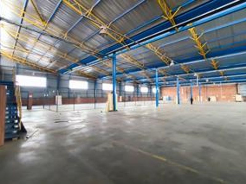 Large open-plan industrial warehouse space featuring high ceilings with exposed steel trusses, concrete flooring, and ample natural light through side windows.