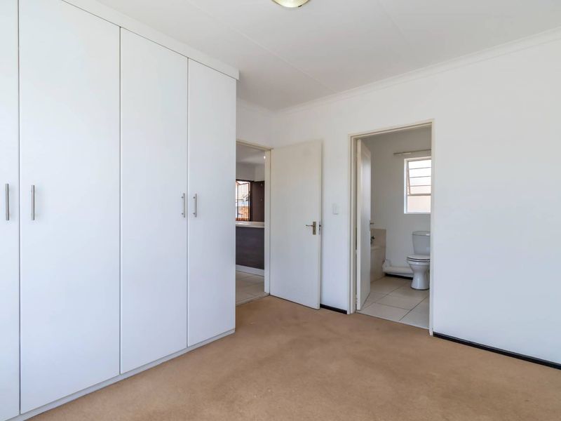 A clean, empty bedroom featuring built-in cupboards, carpeted flooring, and direct access to an en-suite bathroom.