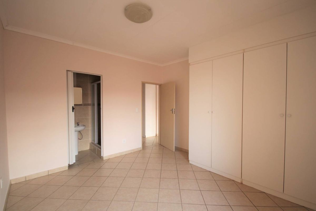 A spacious, empty bedroom featuring neutral tiled flooring, built-in cupboards, and direct access to an en-suite bathroom.
