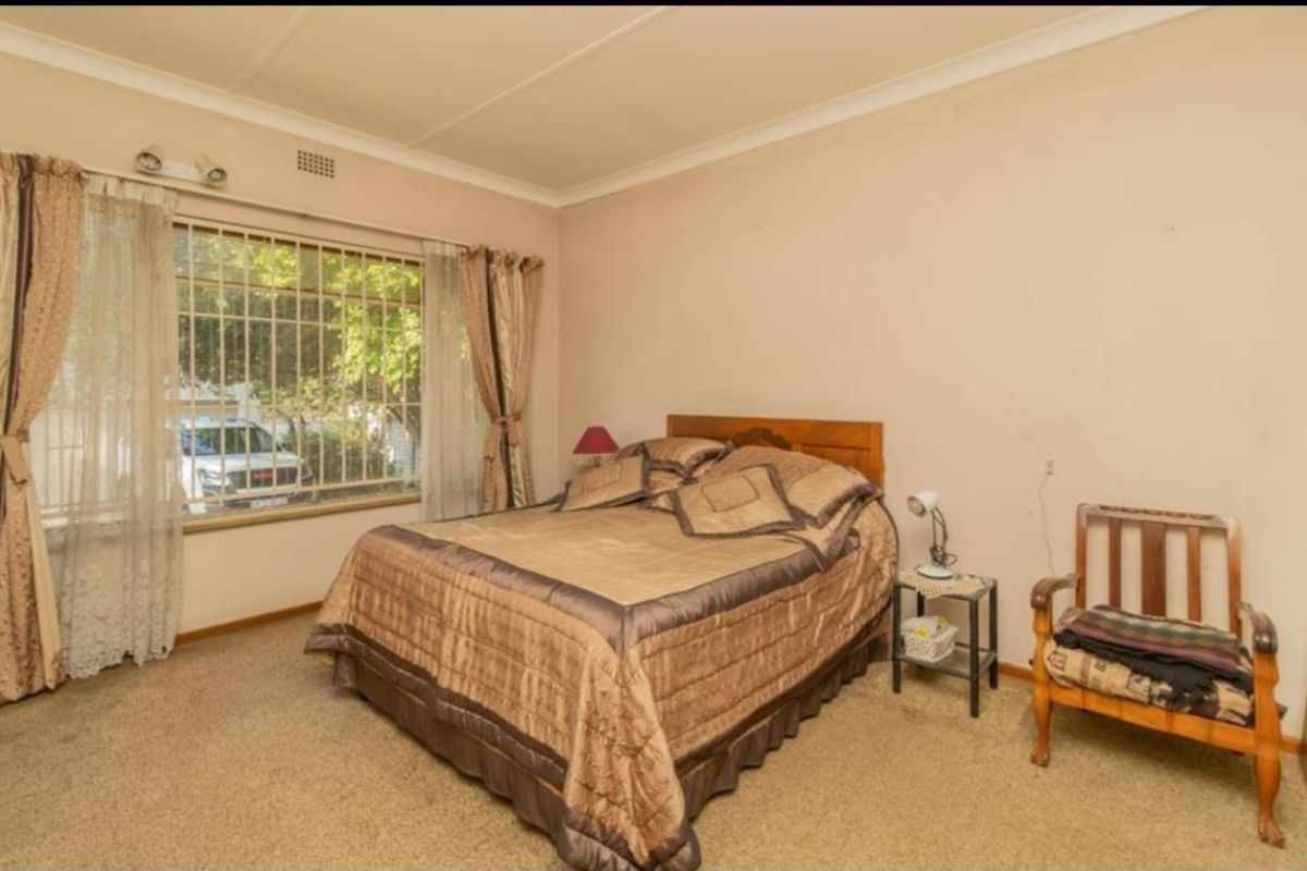 A bedroom featuring a large window with security bars, neutral wall finishes, and carpeted flooring.