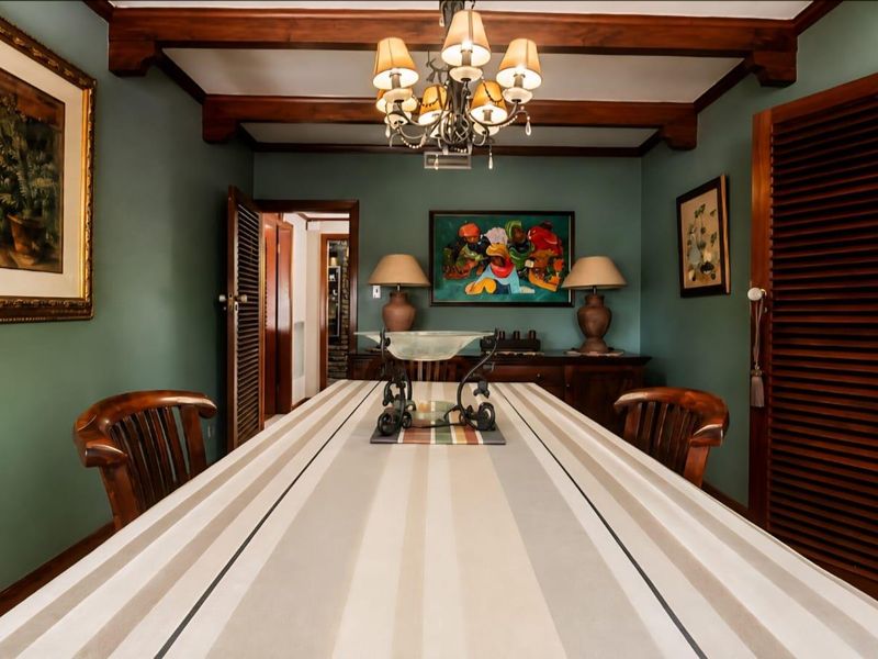 A formal dining room featuring exposed timber ceiling beams, louvered wooden doors, and a classic chandelier, creating a warm and traditional atmosphere.