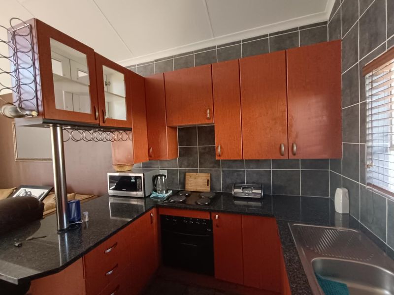 A functional kitchen featuring dark granite countertops, wood-finish cabinetry, a built-in electric oven and hob, and a tiled backsplash.