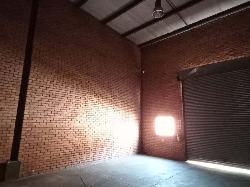 Spacious industrial warehouse unit featuring high ceilings, exposed brick walls, concrete flooring, and a large roller shutter door for easy access.