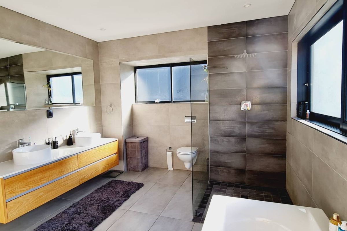 Modern bathroom featuring a double vanity with wooden cabinetry, a spacious walk-in shower with glass screen, and a wall-mounted toilet with neutral tiling.