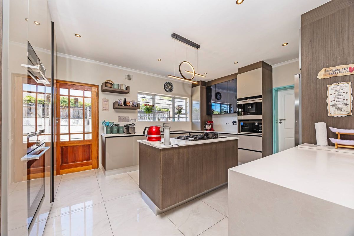 Modern kitchen featuring a central island with a built-in gas hob, sleek cabinetry, integrated oven and microwave, and polished tile flooring.