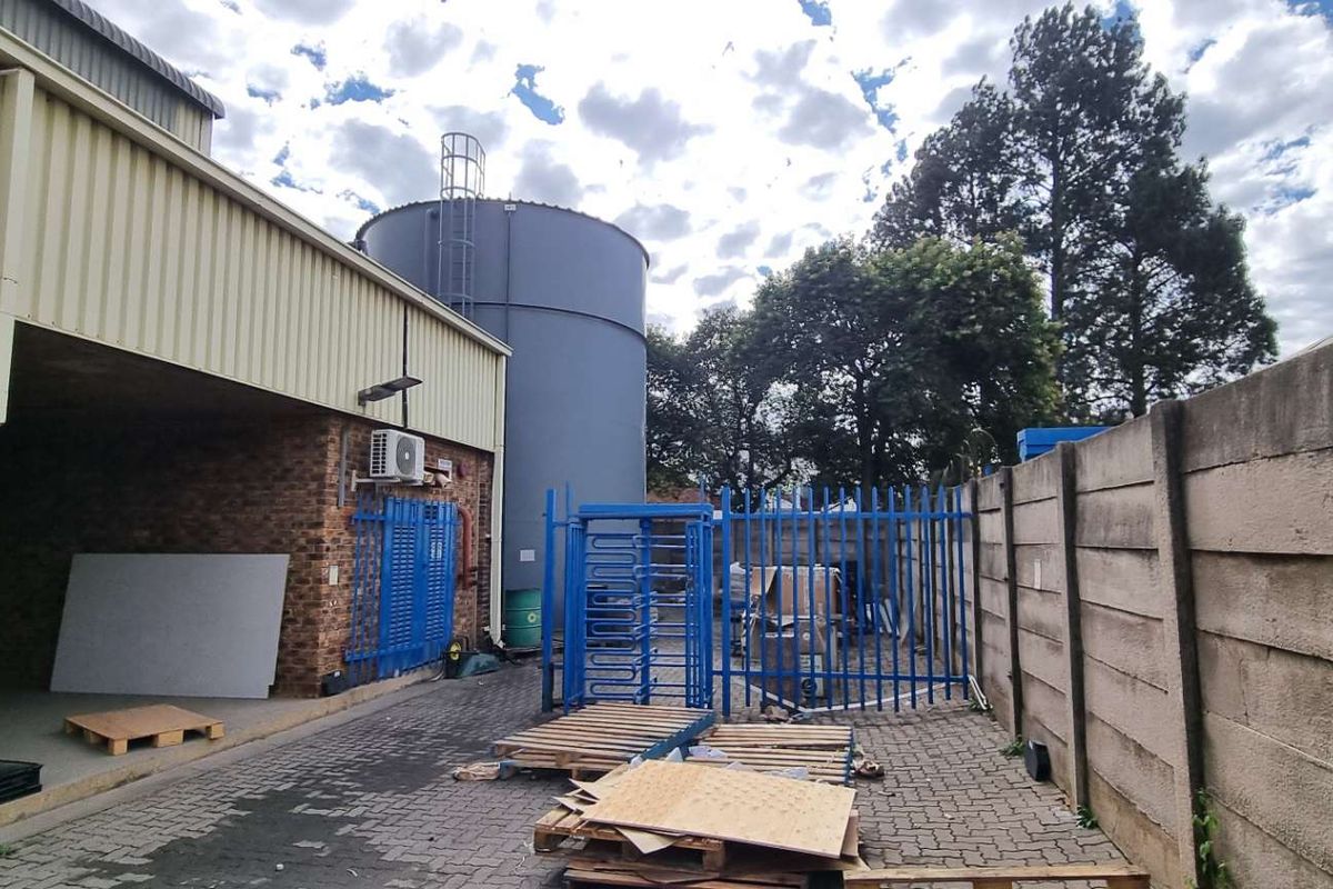 Industrial exterior yard area featuring a large storage tank, secure gated access, and covered loading space with brick and metal cladding construction.