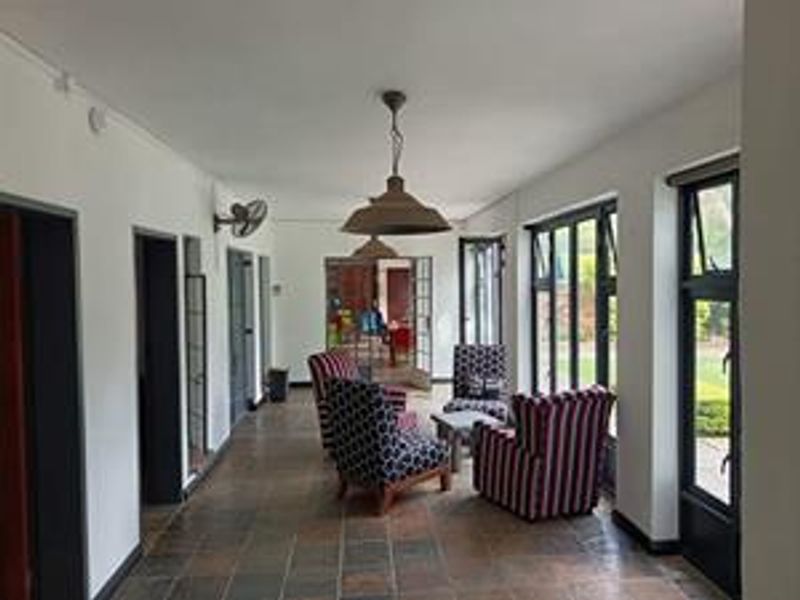 A spacious living area featuring tiled flooring, large windows, and classic pendant lighting, offering a bright and functional space with direct outdoor access.