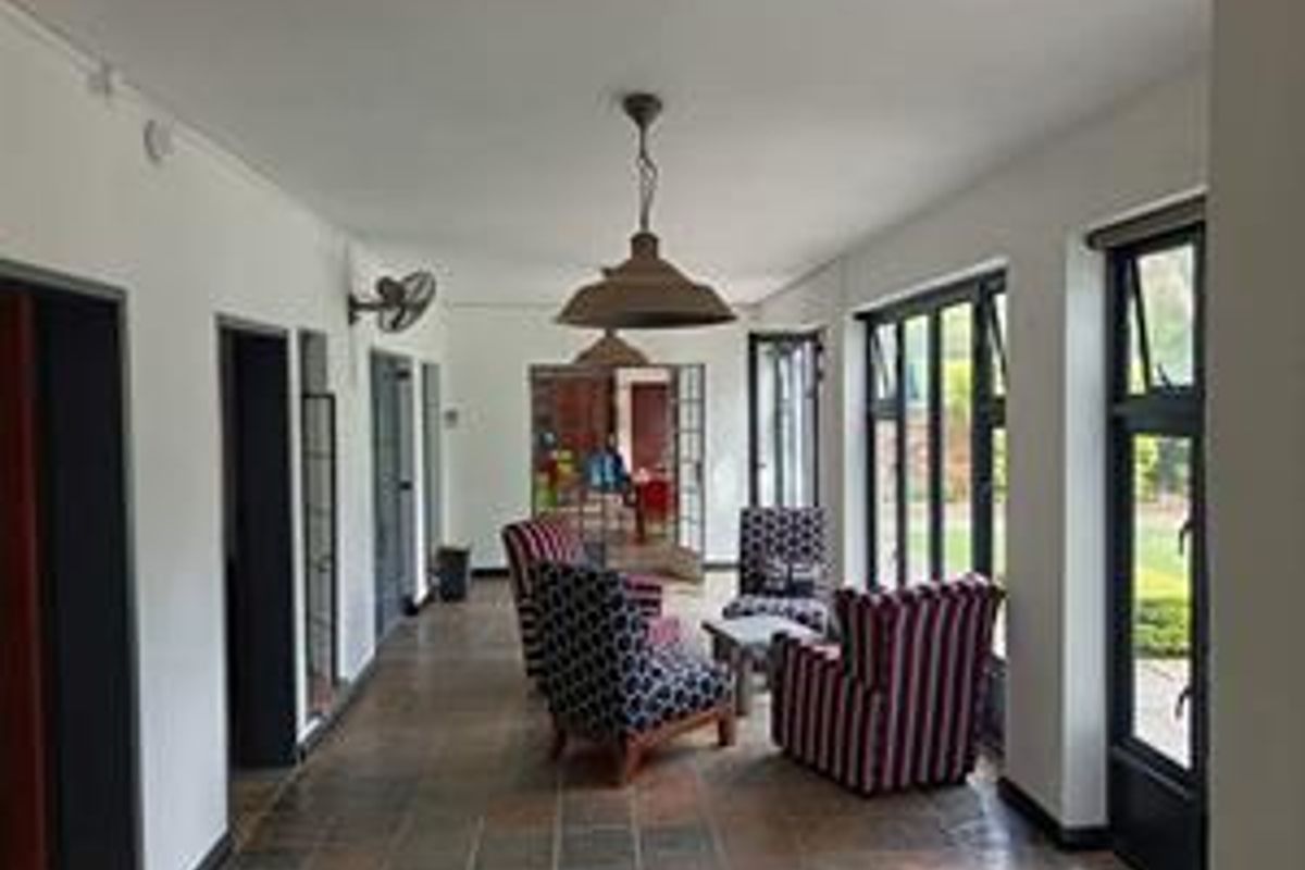 A spacious living area featuring tiled flooring, large windows, and classic pendant lighting, offering a bright and functional space with direct outdoor access.