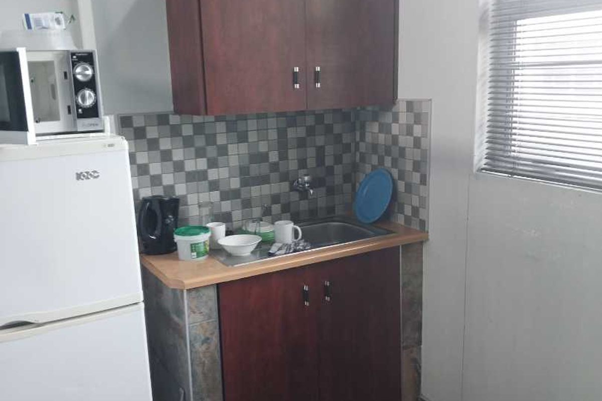 A compact kitchenette area featuring dark wood cabinetry, a tiled backsplash, a stainless steel sink, and stone-style flooring.