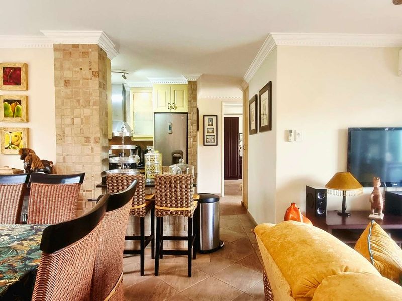 Open-plan living and dining area featuring tiled flooring, crown molding, and a tiled feature pillar, seamlessly connecting to the kitchen space.