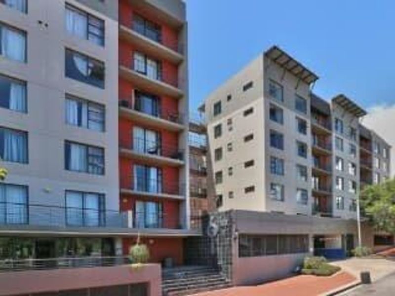 A modern multi-story apartment complex featuring a contemporary facade with balconies, metal railings, and a paved entrance area.