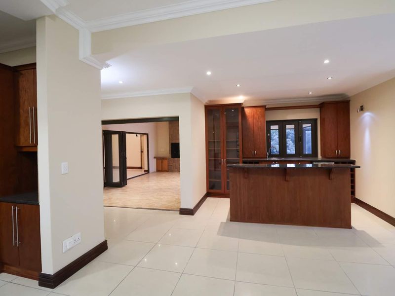 Spacious open-plan kitchen featuring rich wooden cabinetry, granite countertops, and a central island, seamlessly flowing into the adjacent living area.